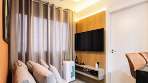 Een moderne woonkamer met een bank, een flatscreen televisie aan de muur en een koffieapparaat op een houten console.