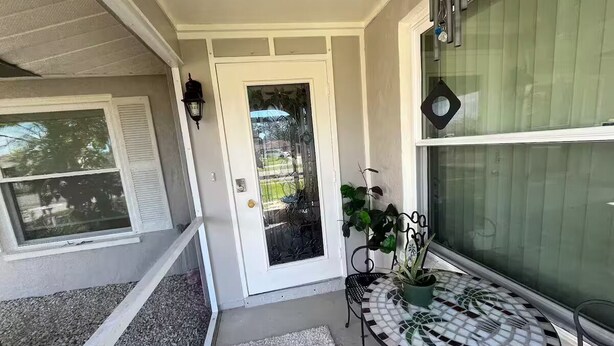 Un porche abrité avec une porte, une petite table sur laquelle est posée une plante en pot et une fenêtre avec des stores.