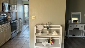 Une cuisine équipée d’appareils électroménagers modernes, une console blanche agrémentée d’objets décoratifs et un tableau encadré au mur.