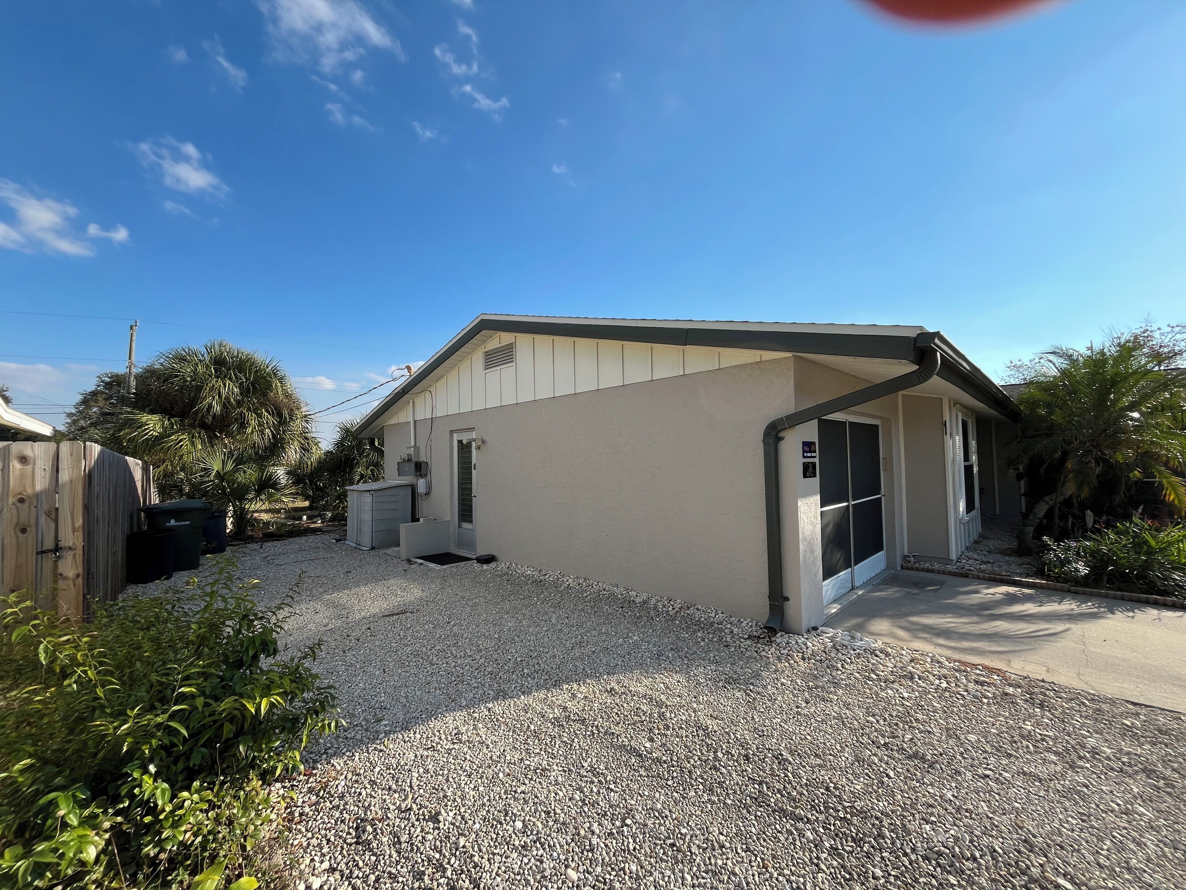 A single-story building with a gravel driveway, a covered outdoor area, and a fenced backyard.