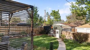Ein Garten mit Holzzaun, Rasenfläche, einer kleinen Gartenhütte und einem Haus im Hintergrund.