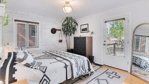 Ein Schlafzimmer mit einem Bett, einem Schminktisch, einer Pflanze und einer Tür, die auf einen Balkon führt.