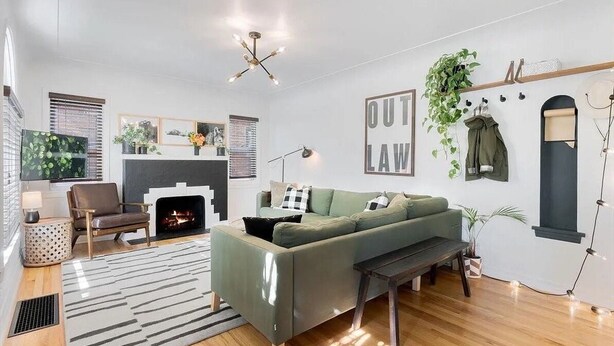 Ein modernes Wohnzimmer mit einem grünen Sofa, einem Kamin, einer hängenden Pflanze und einem Schild an der Wand mit der Aufschrift 'OUT LAW'.