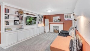 Ein Wohnzimmer mit Flachbildfernseher, weißen Einbauschränken, einem Kamin und einer Couch.