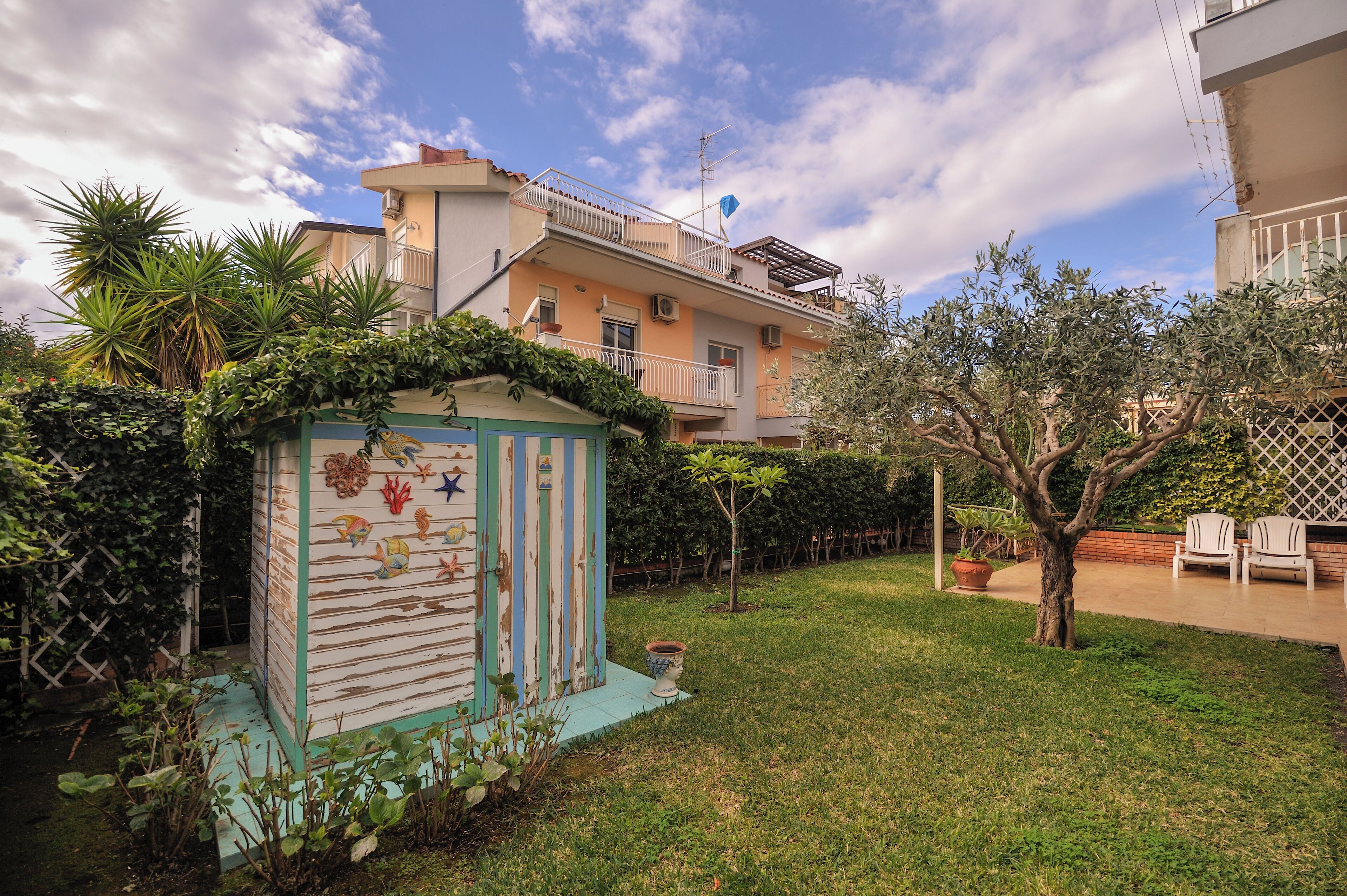 A residential area with a small garden, a colorful shed, and a two-story building with balconies.