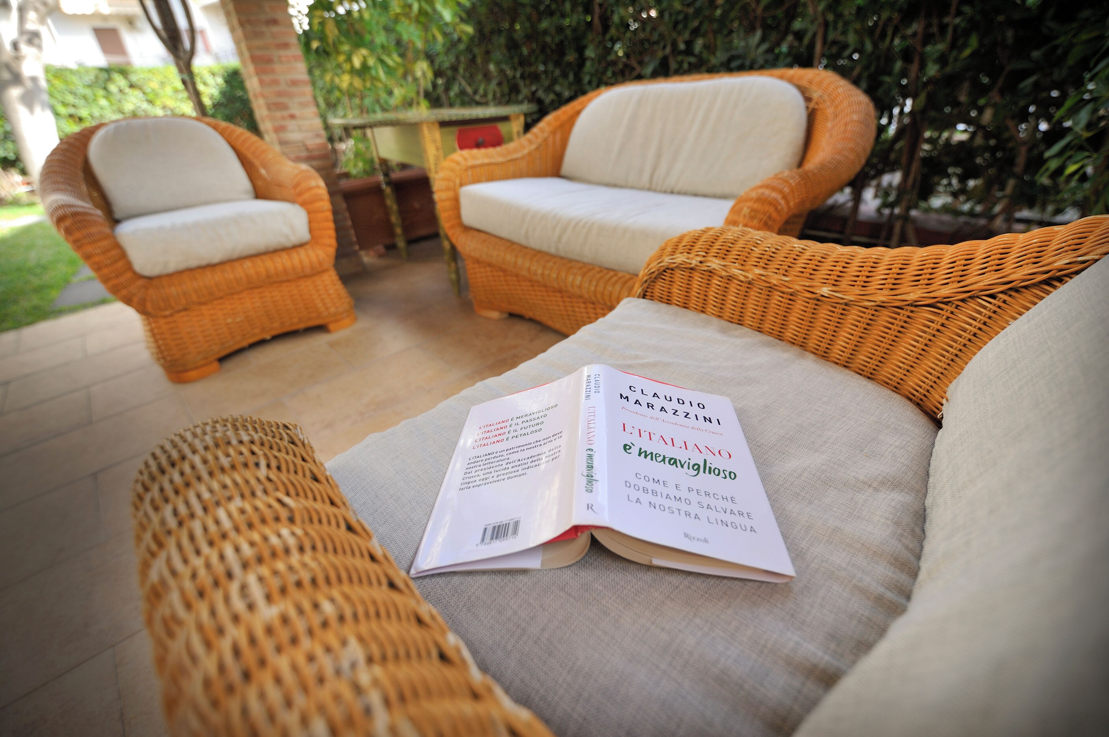 A wicker sofa with a book titled 'L'ITALIANO è meraviglioso' placed on it.