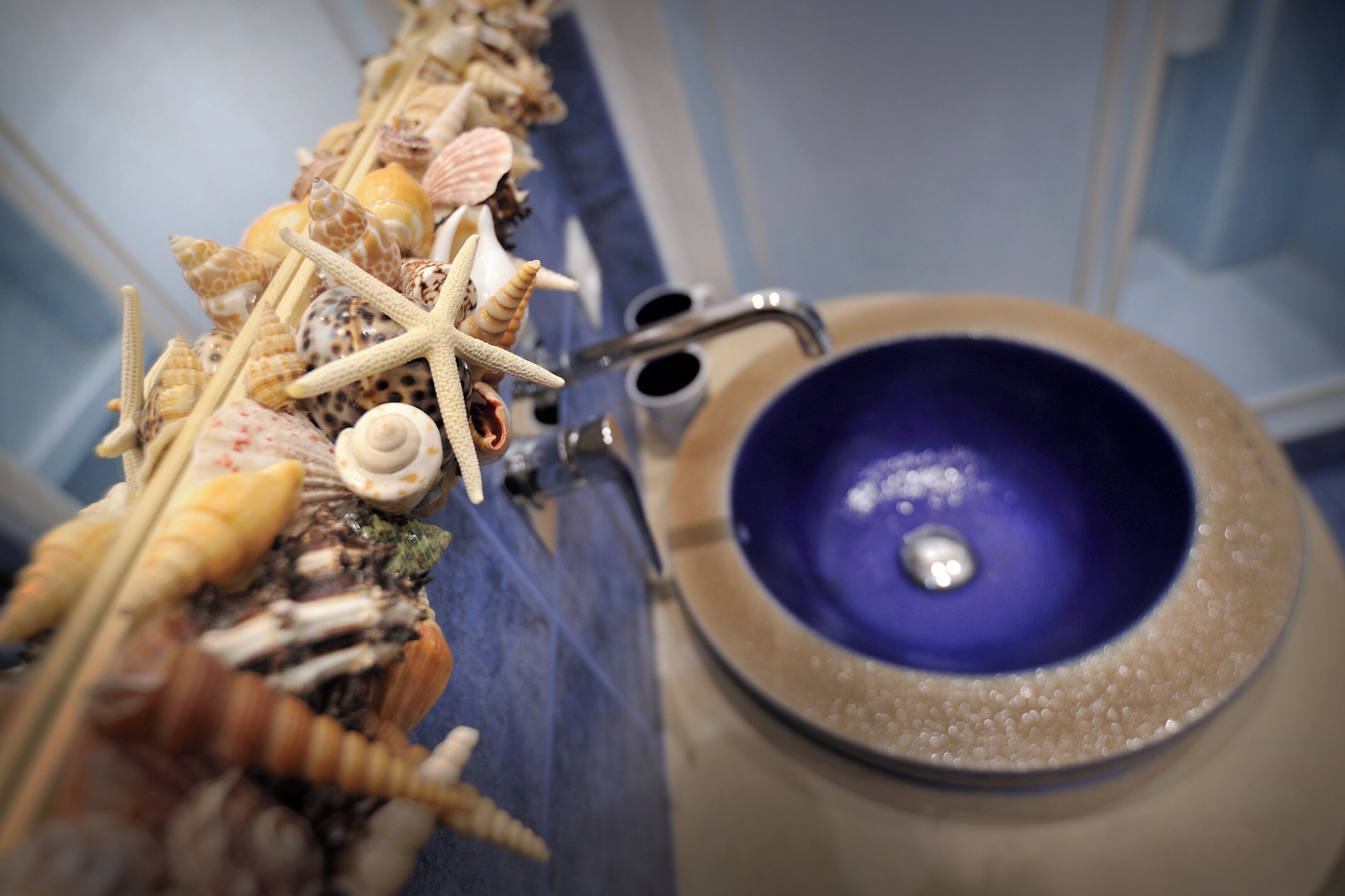 Un bagno con un lavandino blu e una parete decorata con conchiglie e stelle marine.