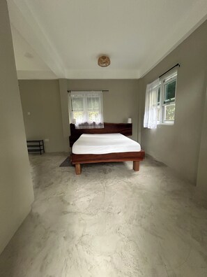 A bedroom with a wooden bed, a window with curtains, and a concrete floor.
