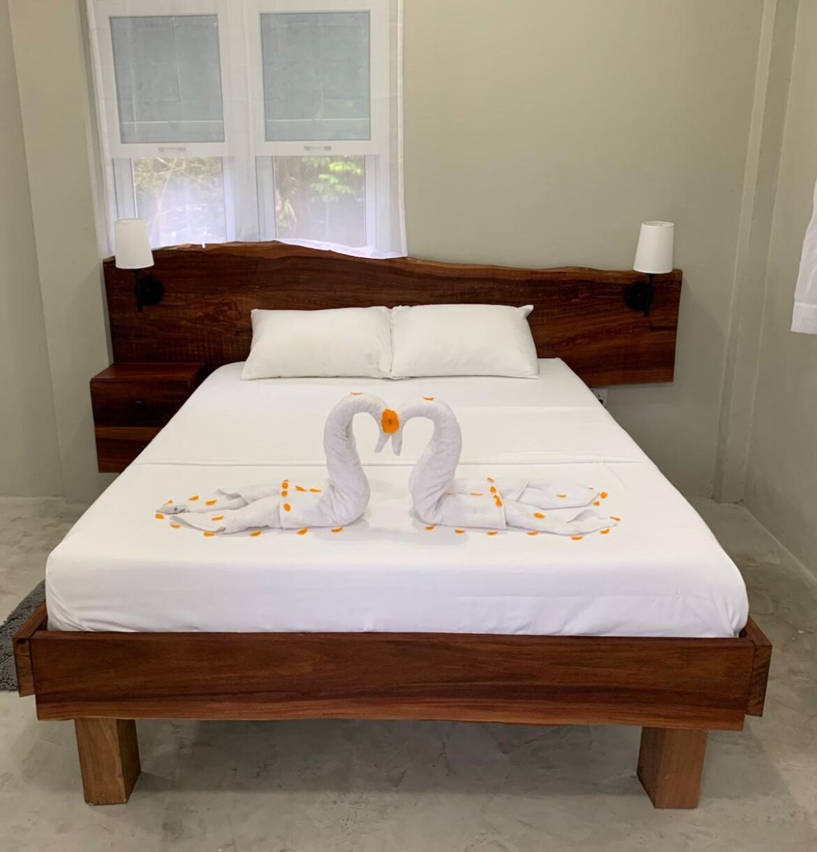 Una cama bien hecha con cabecera de madera, ropa blanca y una decoración de toallas con forma de cisne.