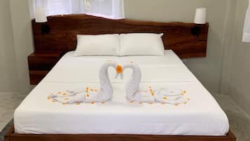 Una cama bien hecha con cabecera de madera, ropa blanca y una decoración de toallas con forma de cisne.