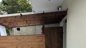 A patio with two wicker chairs and a table, a wooden fence, and a white wall.