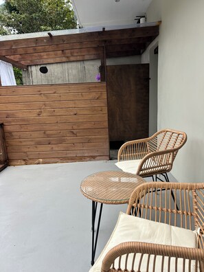 A patio with two wicker chairs and a table, a wooden fence, and a white wall.