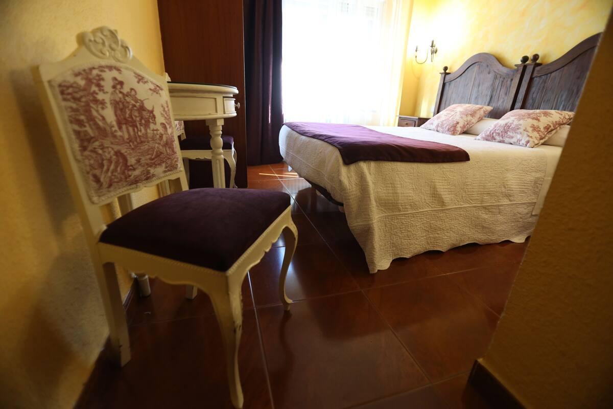 Ein Schlafzimmer mit Bett, Stuhl, kleinem Tisch und Wandlampe.