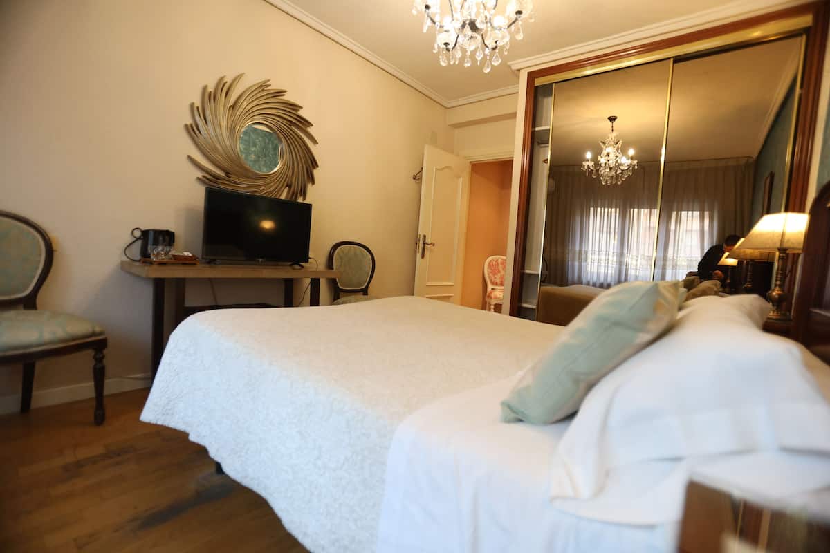 Ein Hotelzimmer mit einem großen Bett, einem Fernseher, einem Schreibtisch mit Stuhl und einem Spiegel.