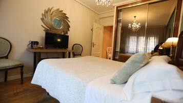 Una habitación de hotel con una cama grande, televisión, escritorio con silla y espejo.