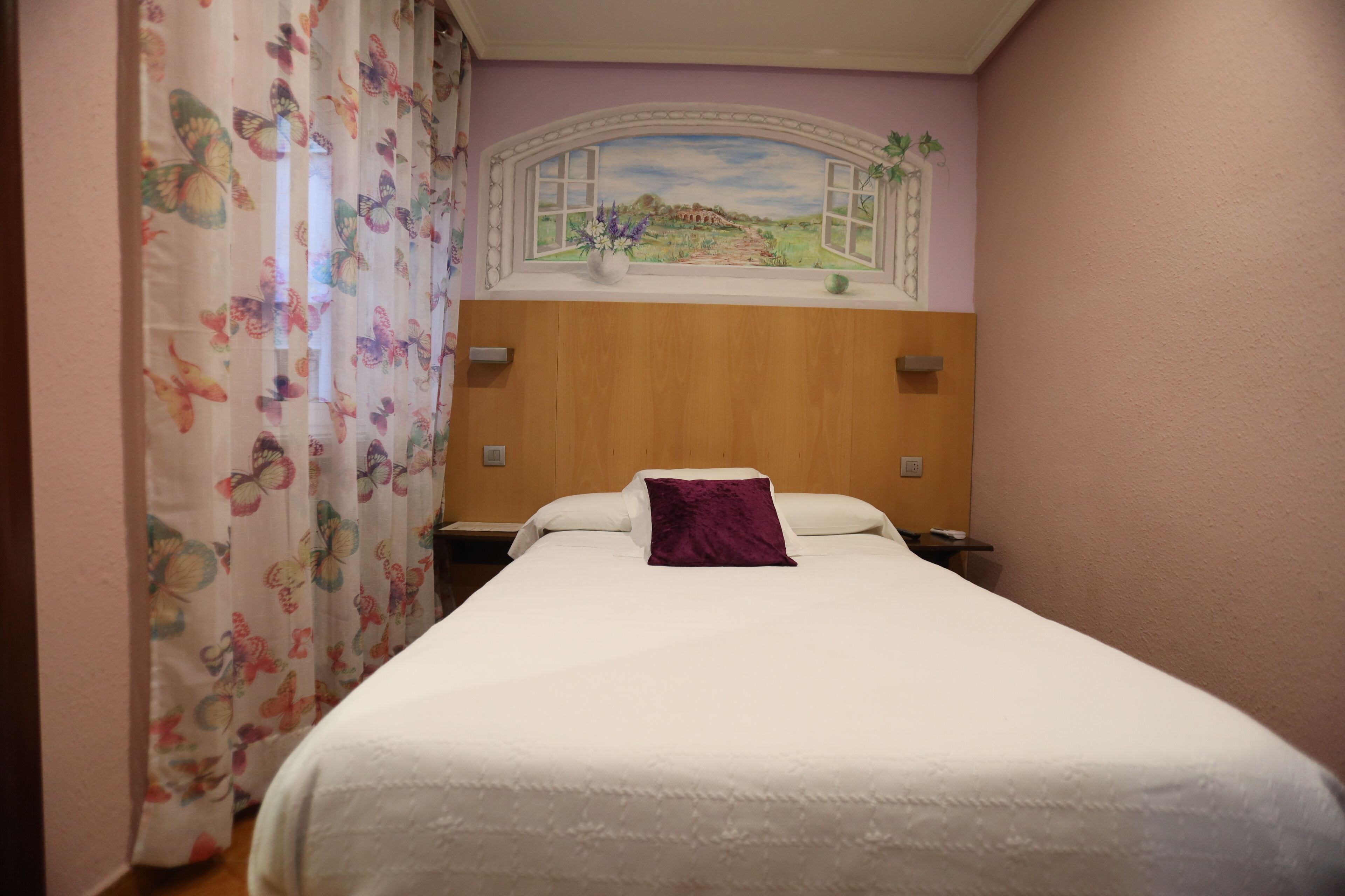 A bedroom with a bed, a window with a view of a landscape, and a curtain with a butterfly pattern.