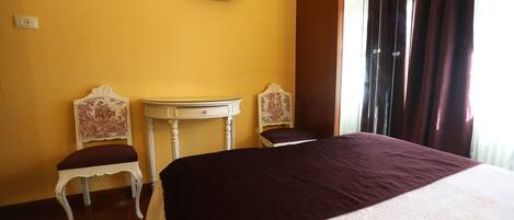A hotel room with a bed, two chairs, a small table, a television on the wall, and a window with curtains.