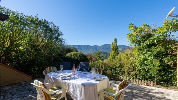 Une table ronde installée à l’extérieur, avec des chaises, un sol en pierre et une vue sur les montagnes.