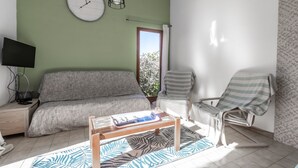 Une pièce comprenant un canapé, un fauteuil, une petite table, une horloge et un téléviseur posé sur un meuble.