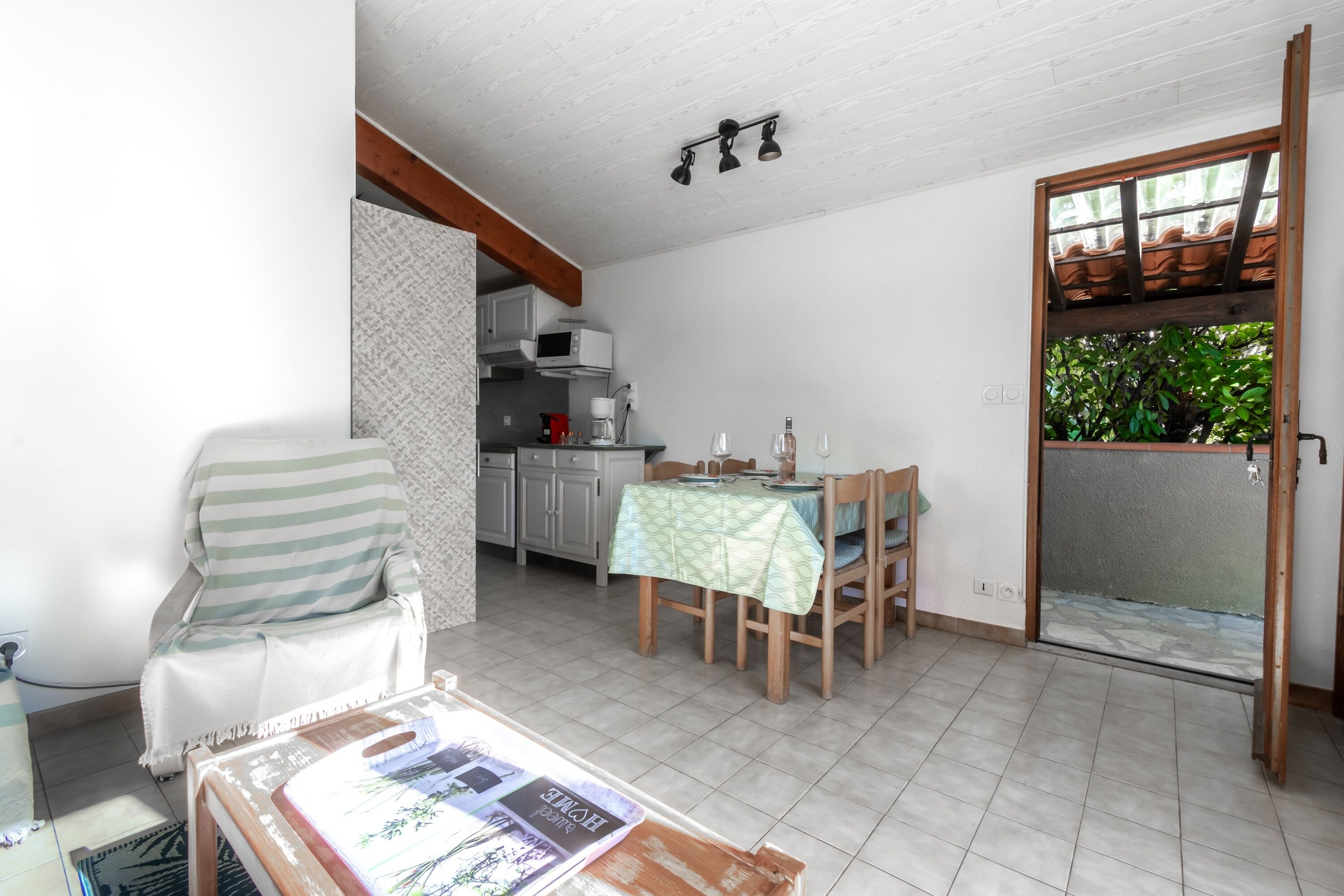 A dining area with a table set for two, a chair, and a kitchen in the background.