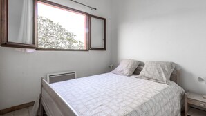 Une chambre à coucher avec un lit, une table de chevet, une fenêtre avec des rideaux et un radiateur.