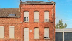 Een gebouw van rode baksteen met meerdere ramen, waarvan sommigen voorzien zijn van luiken, en een klein balkon.