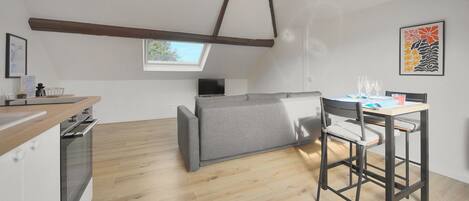 A modern kitchen with a built-in oven, a dining area with a table and chairs, a grey sofa, and a skylight.