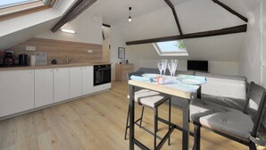 Een moderne keuken met dakraam, houten balken, een eethoek met tafel en stoelen, en een gezellige zithoek.