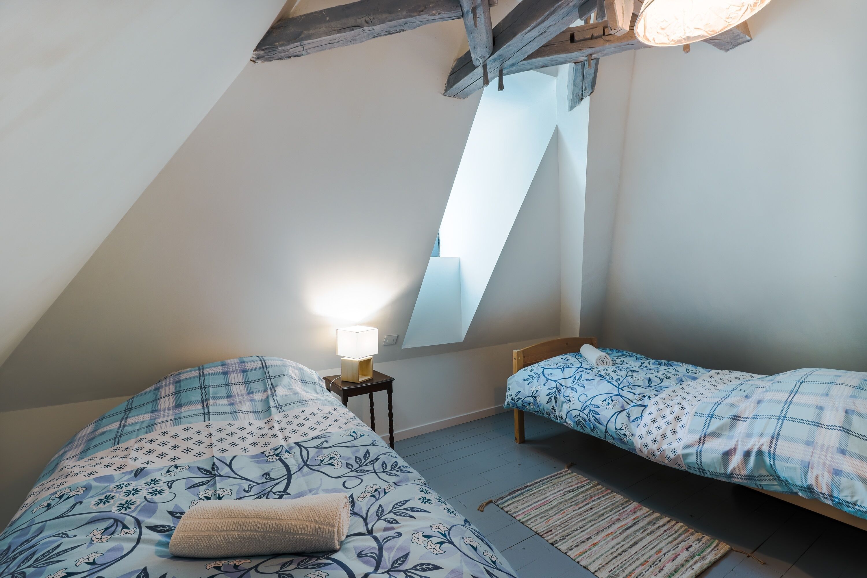 Een slaapkamer met twee bedden, een dakraam en een nachtkastje met een lamp.