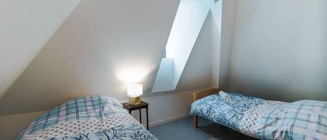 Een slaapkamer met twee bedden, een dakraam en een nachtkastje met een lamp.