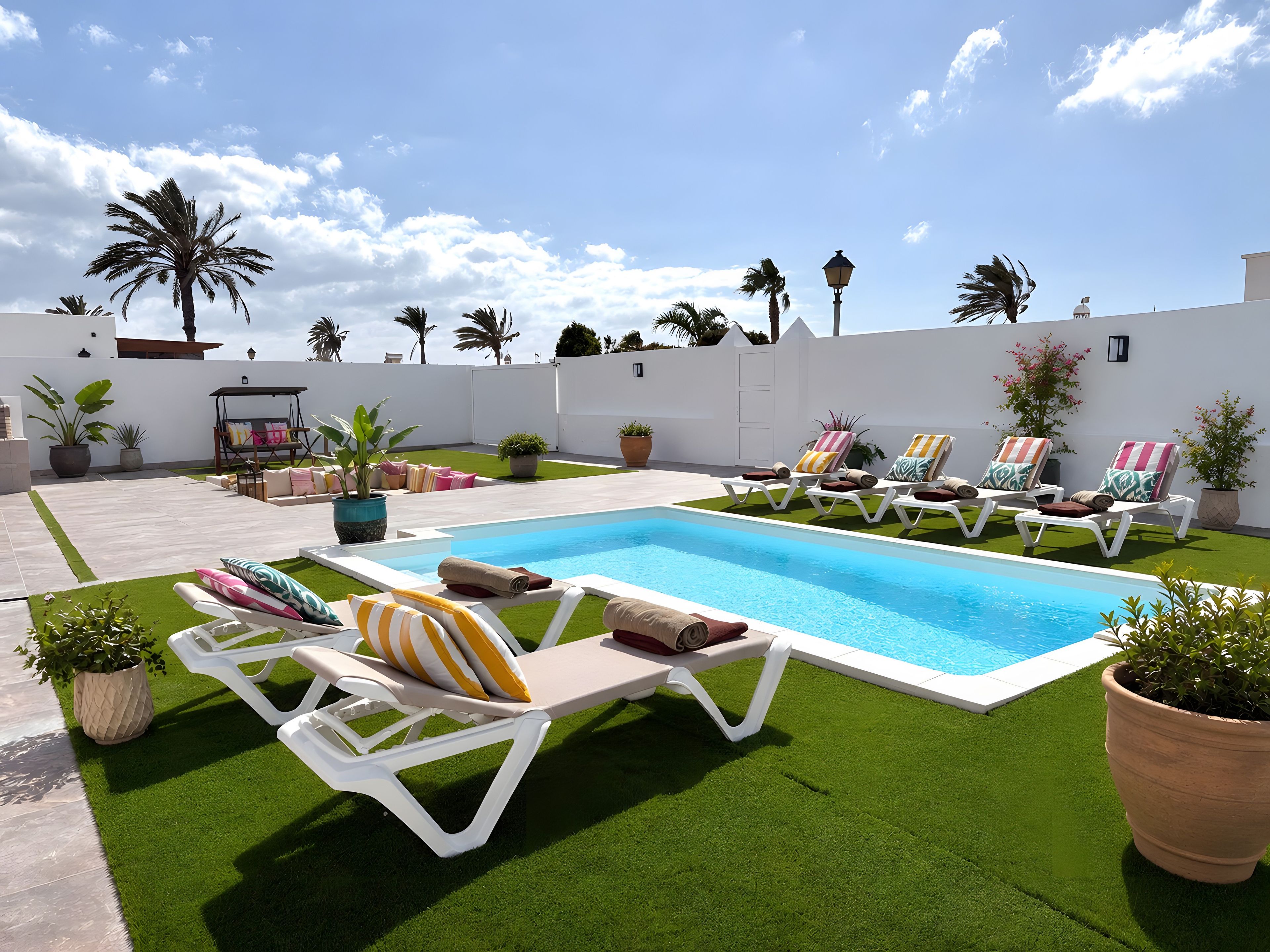 A pool area with artificial grass, lounge chairs, and potted plants.