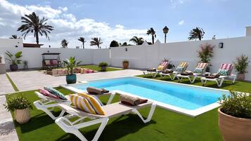 A pool area with artificial grass, lounge chairs, and potted plants.