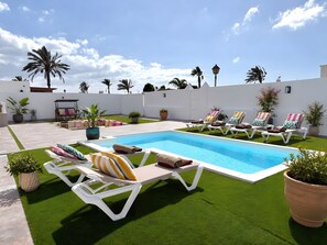 Un espace piscine agrémenté de gazon synthétique, de chaises longues et de plantes en pot.