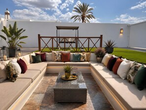 Un espacio exterior moderno con zona de estar, sofá, cojines y una mesa de centro.