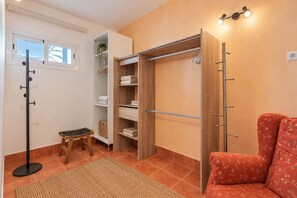 Quarto com guarda-roupa de madeira, um banquinho pequeno, sofá vermelho e luminária de chão.
