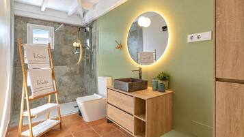 Un baño con tocador de madera, inodoro blanco, cabina de ducha de vidrio y un perchero con toallas de 'The Suite Villa'.
