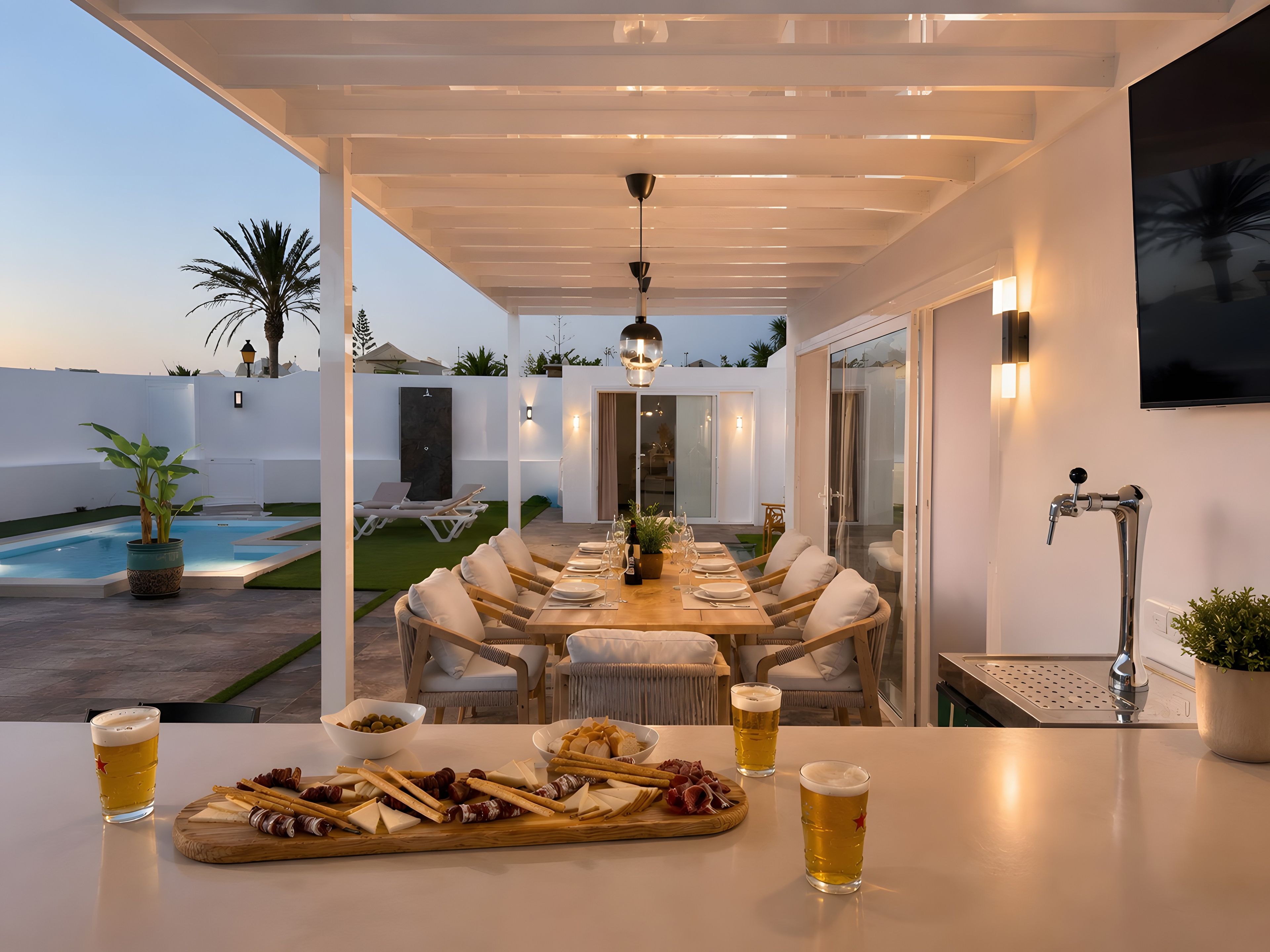 An outdoor dining area with a pool, lounge chairs, and a table set for two with a variety of cheeses and crackers.
