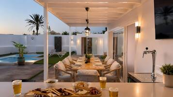 An outdoor dining area with a pool, lounge chairs, and a table set for two with a variety of cheeses and crackers.