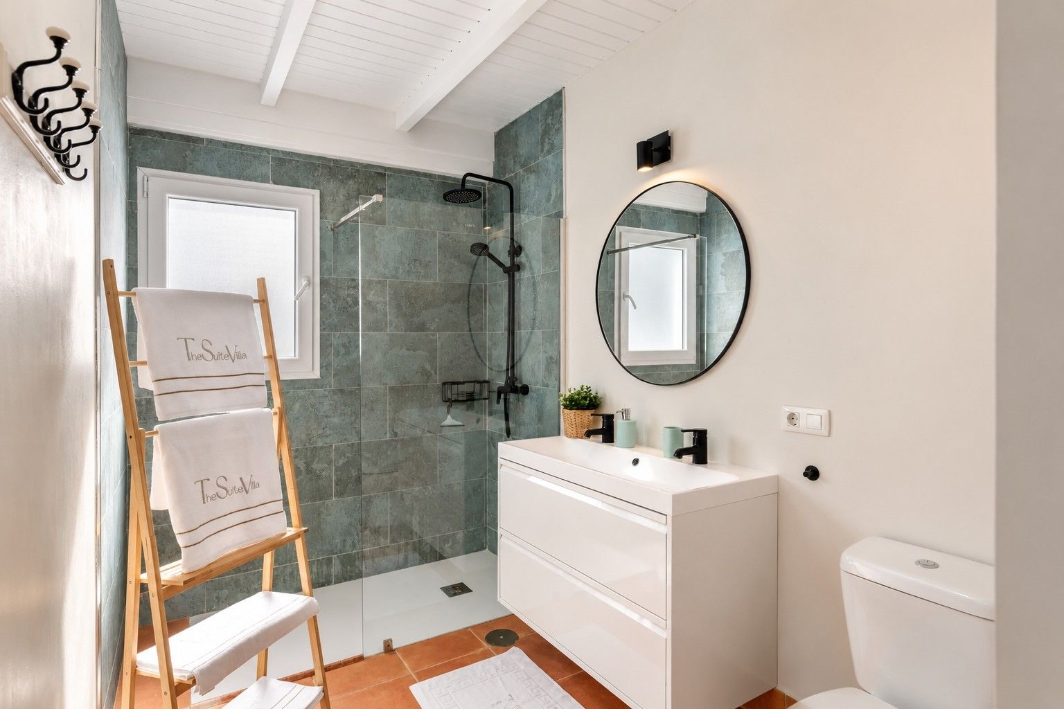 A modern bathroom with a shower, a sink, a toilet, and a wooden ladder with towels.