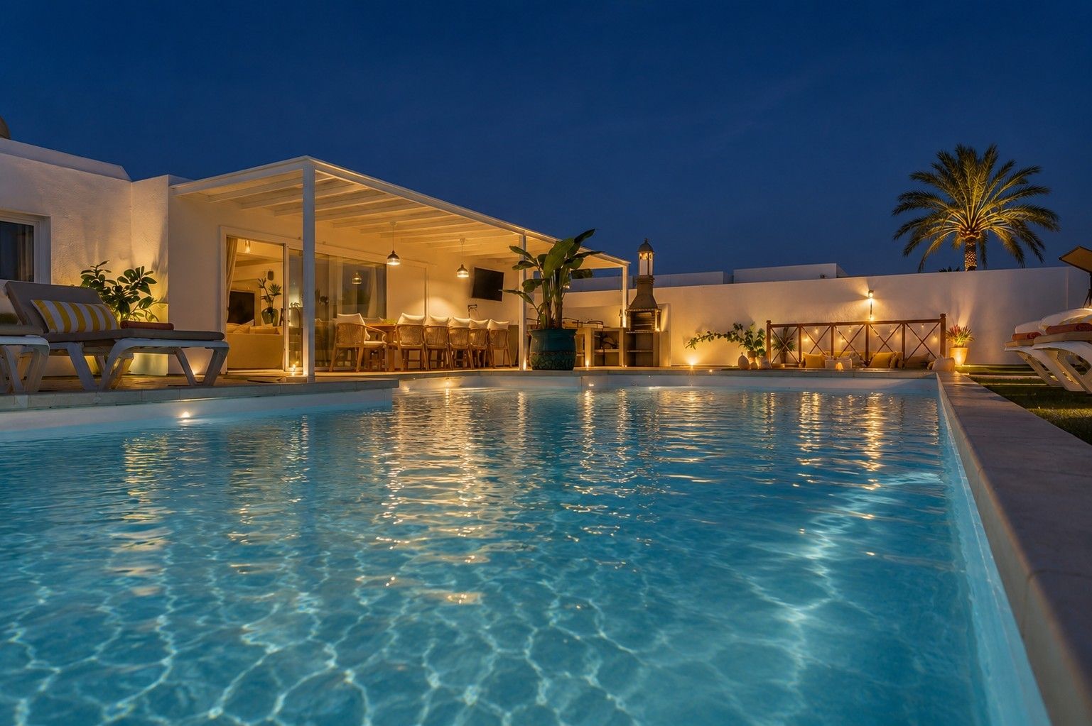 Una piscina con sillones de descanso y un área de estar techada al aire libre.
