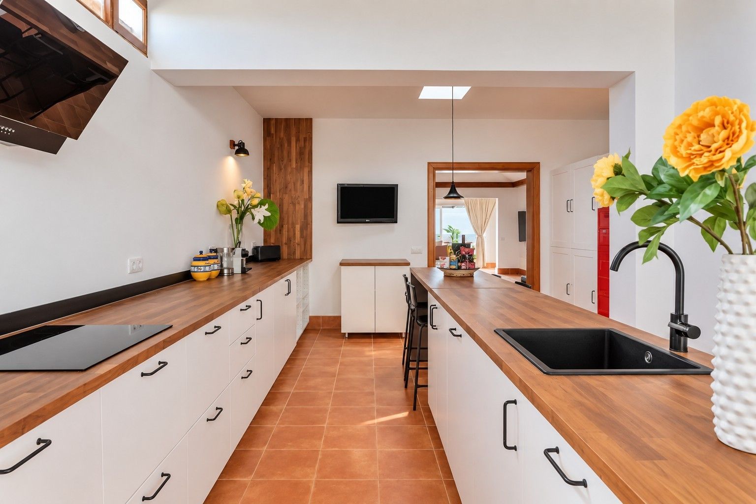 Eine moderne Küche mit einer Holzarbeitsplatte, weißen Schränken, einem schwarzen Spülbecken und einem flachbildschirmfernseher an der Wand.