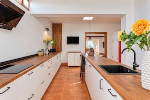 A modern kitchen with a wooden countertop, white cabinets, a black sink, and a flat-screen TV mounted on the wall.