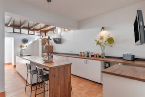 A modern kitchen with a wooden island, bar stools, a built-in oven, and a large window.