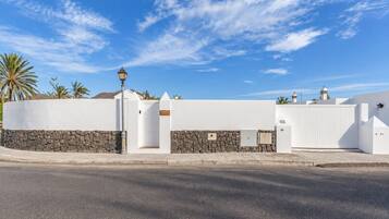 Un edificio blanco con base de piedra, entrada protegida por una reja y un farol.