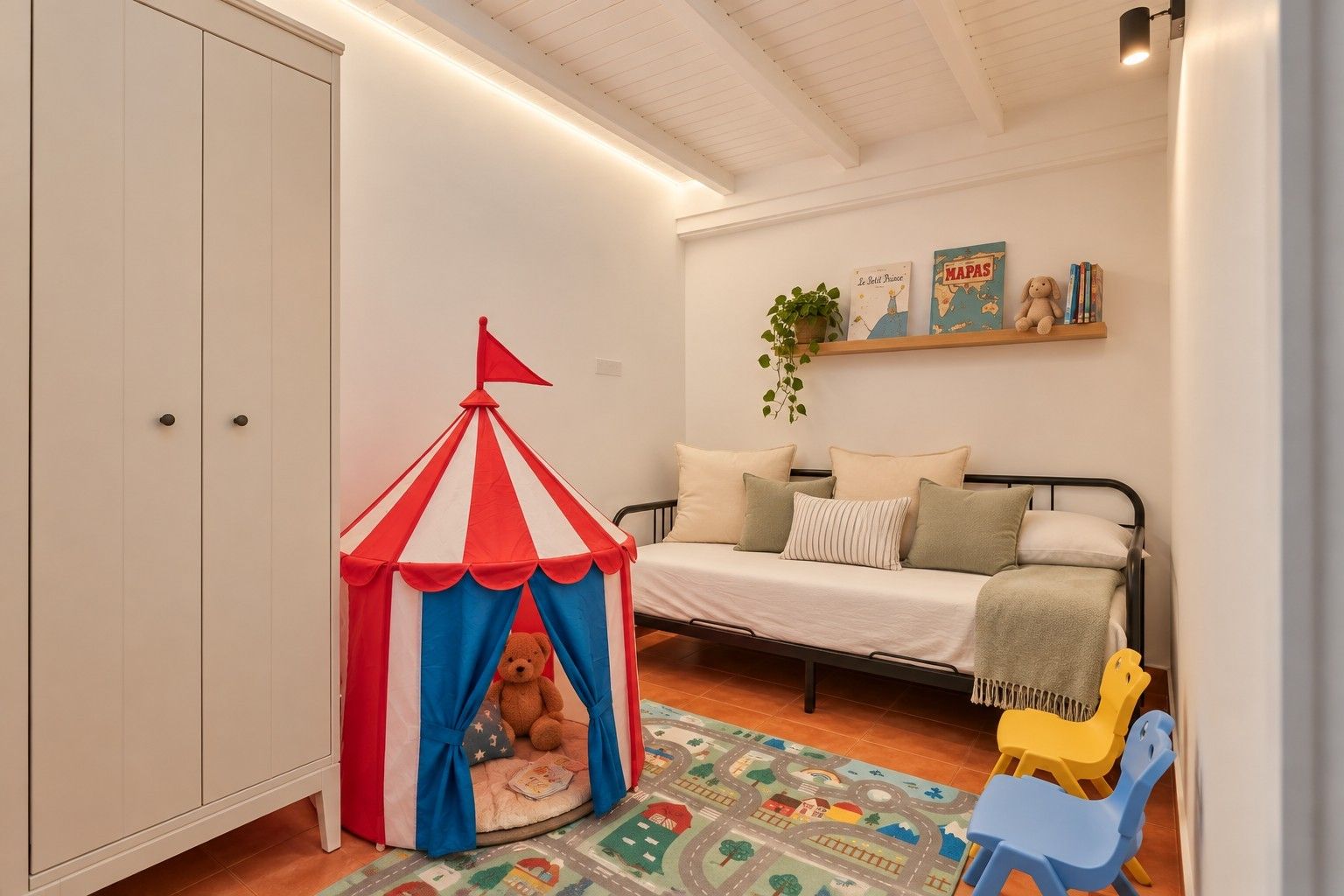 Une tente de jeu pour enfants avec un ours en peluche à l’intérieur, un lit avec des oreillers, une petite étagère avec des livres et une plante, et un tapis coloré.
