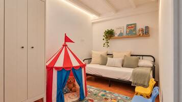 Una carpa infantil con un osito de peluche en su interior, una cama con almohadas, un estante pequeño con libros y una planta, y una alfombra colorida.
