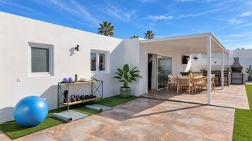 Un patio exterior moderno con zona de estar techada, equipo de ejercicio y una parrilla.