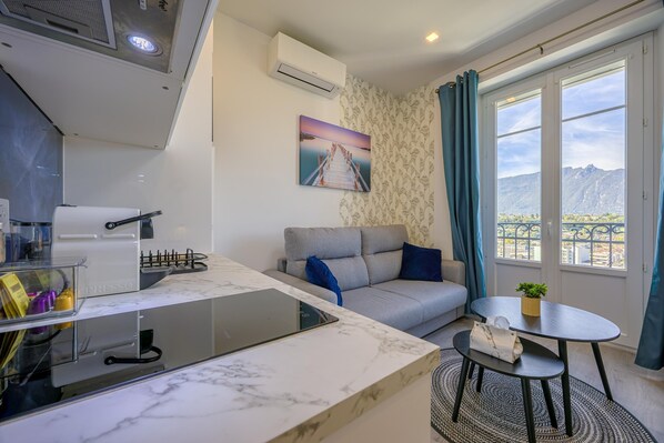 A modern living room with a sofa, a small table, and a kitchen area with a marble countertop.
