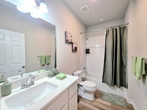 Une salle de bain avec un lavabo blanc, des toilettes, une douche avec un rideau et un miroir.