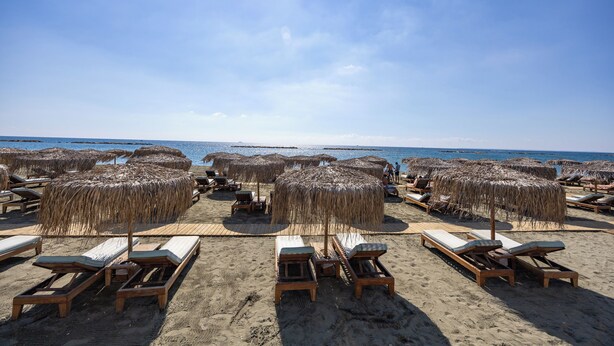 A beach with wooden lounge chairs and straw umbrellas. - Berengaria Court - Sea Views 2bdr Apartment (Limassol)